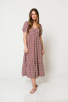 Model in the Maple Field babydoll midi dress in a rosy burgundy gingham check with short puff sleeves and a tiered skirt