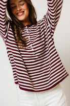 Model with arms raised in the Ever oversized henley sweater with wine and cream horizontal stripes, worn with white pants
