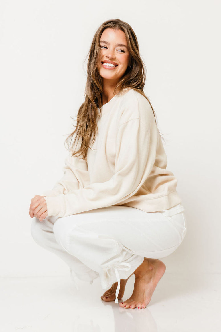 Model crouching in the Zella relaxed pullover sweater in cream, worn with white pants