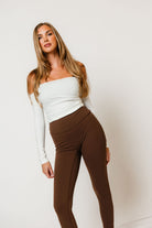 Model in the Cassia soft knit off-the-shoulder top in white with long sleeves, worn with brown leggings