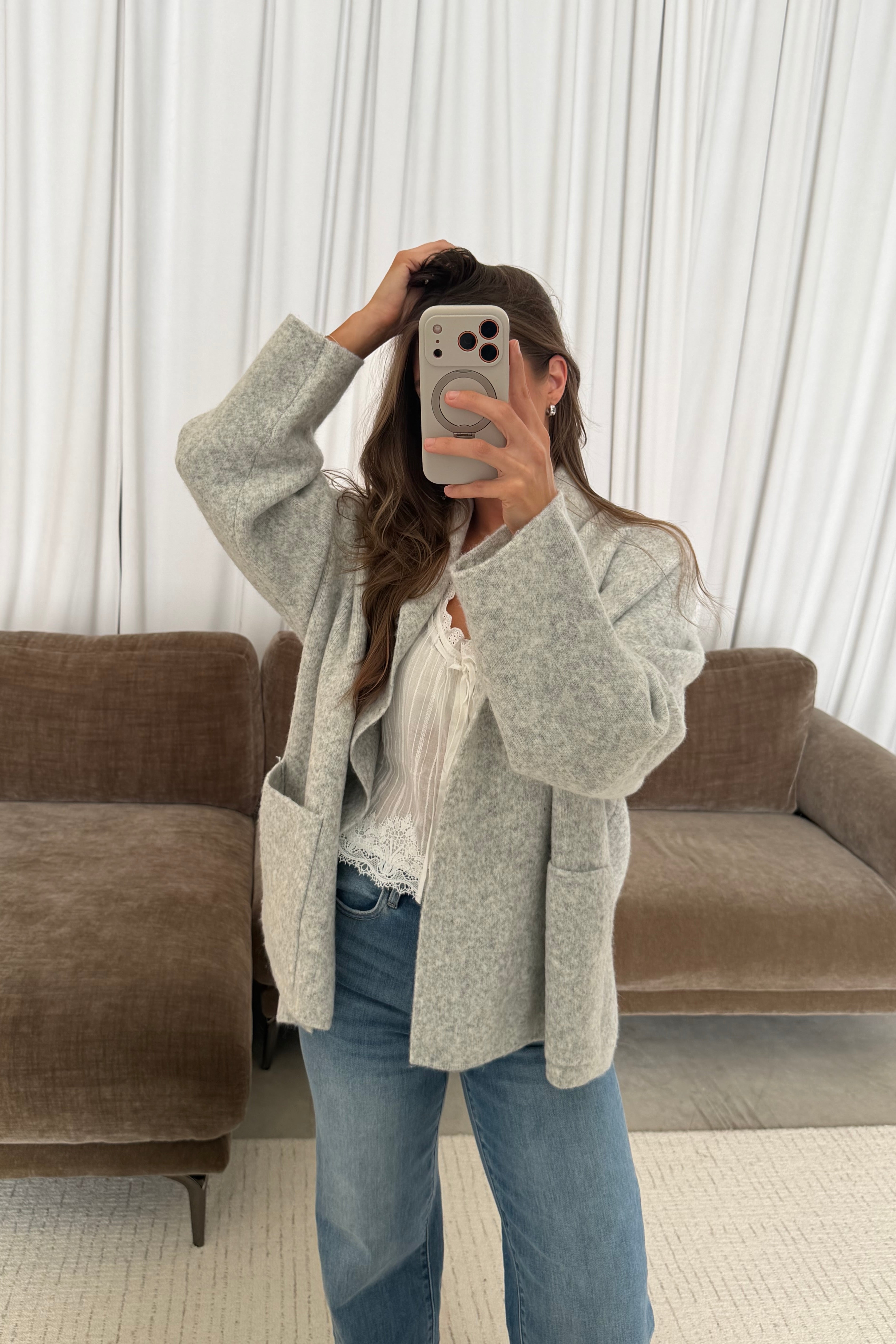 Mirror selfie of a model in the Annabelle relaxed shawl collar open front cardigan in pale birch grey, worn with light jeans