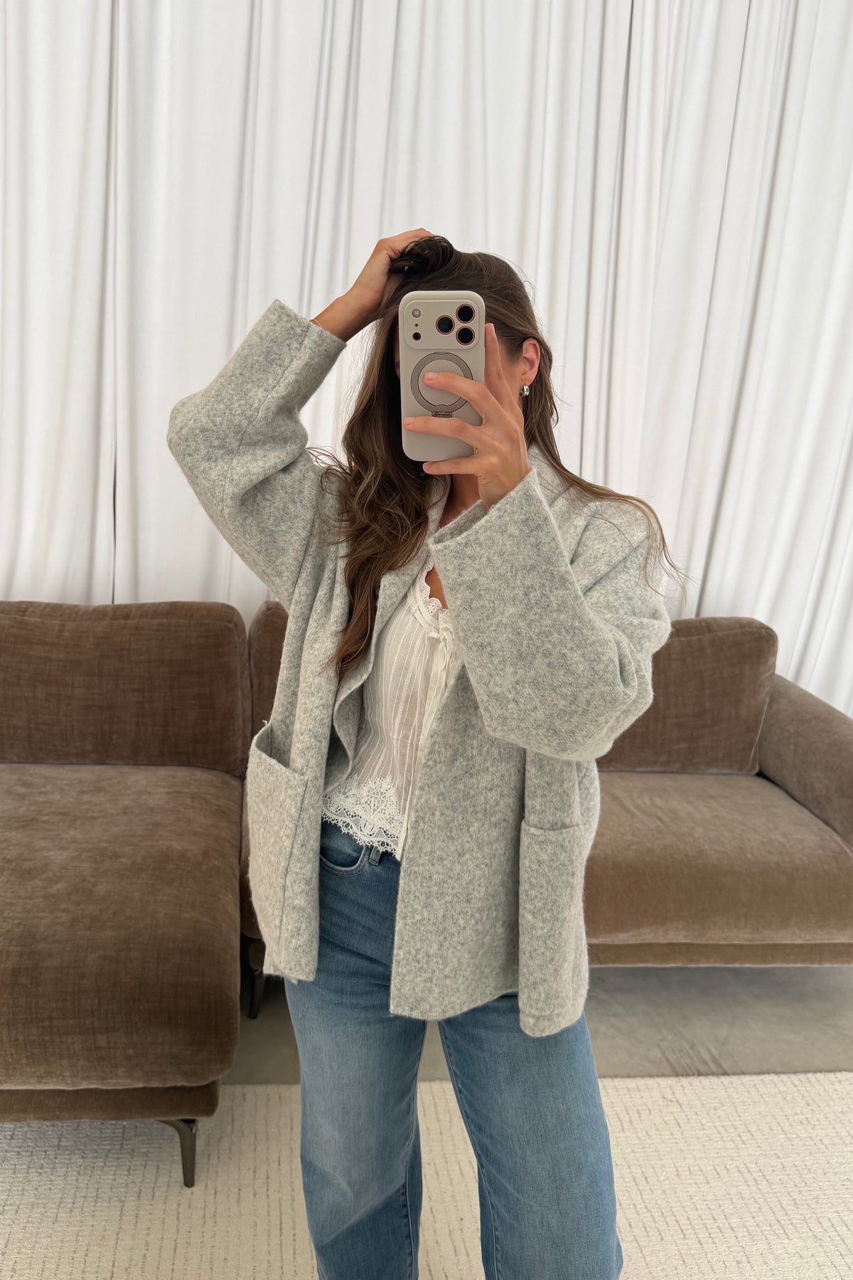 Mirror selfie of a model in the Annabelle relaxed shawl collar open front cardigan in pale birch grey, worn with light jeans